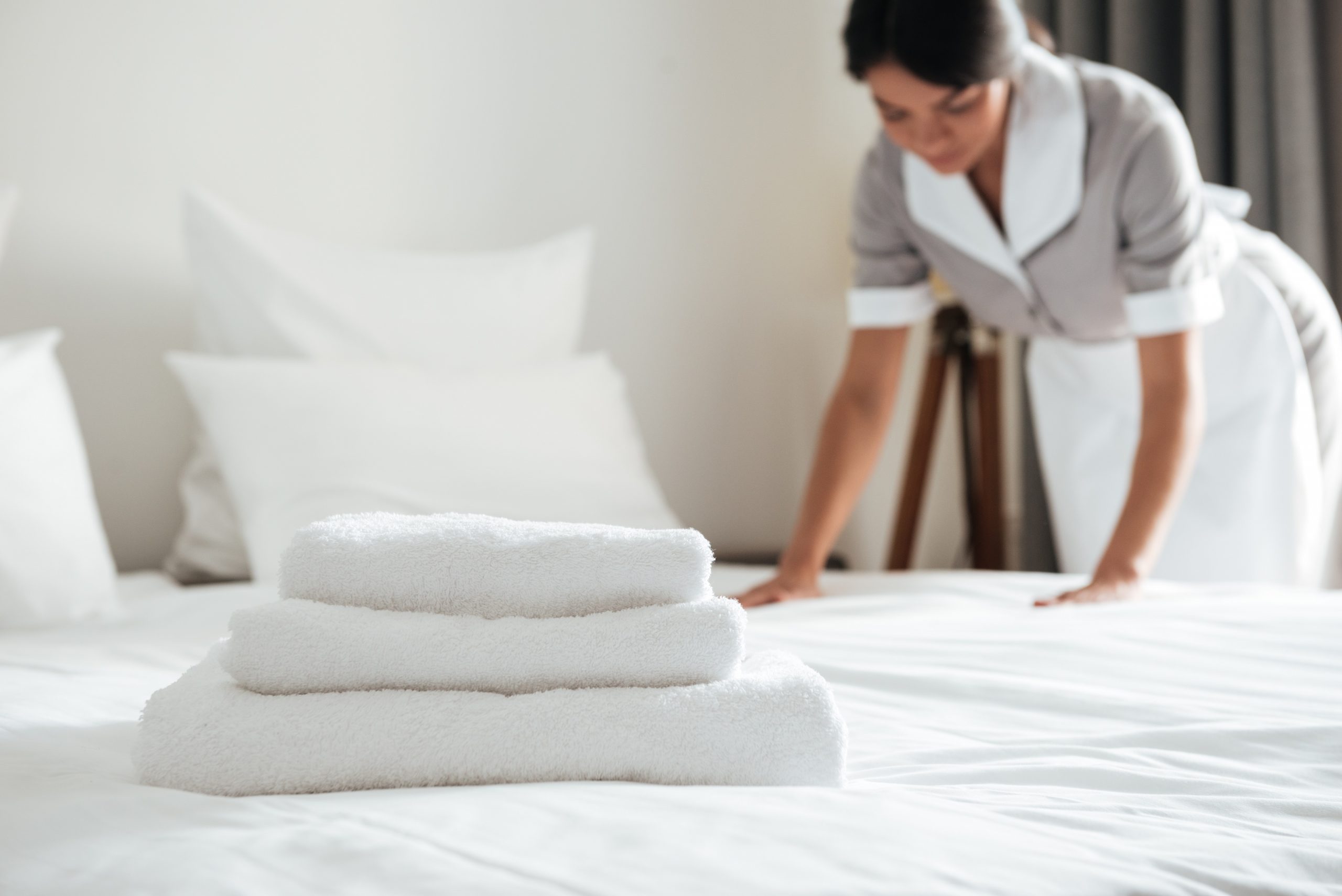 Young hotel maid setting up pillow on bed